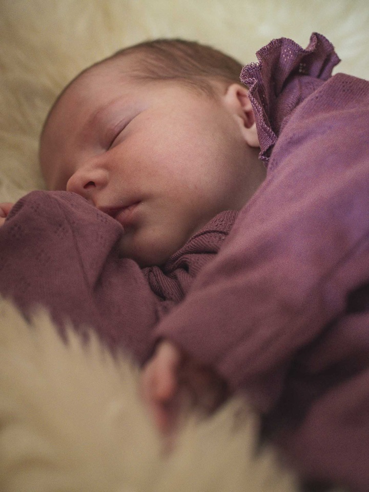 Schlafendes Baby in lila Kleidung auf weichem, hellem Schafsfell. Newbornshooting in und um Geretsried Bad-Tölz Wolfratshausen