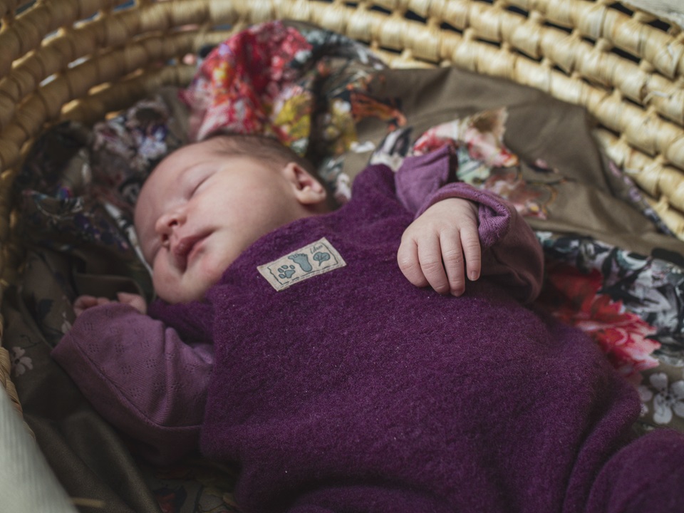 Schlafendes Baby in lila Wollanzug, auf einer bunten Decke liegend. Newbornshooting in und um Geretsried Bad-Tölz Wolfratshausen