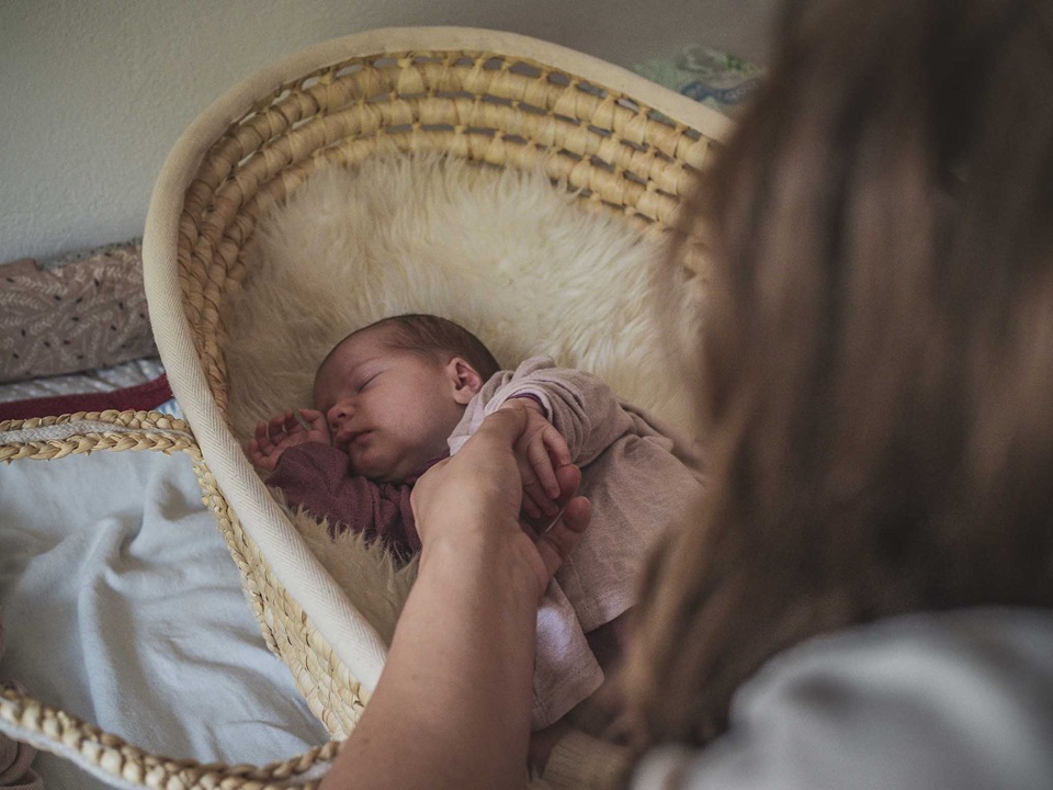 Ein Baby schläft in einem Korb, während die Mutter es sanft umzieht. Newbornshooting in und um Geretsried Bad-Tölz Wolfratshausen