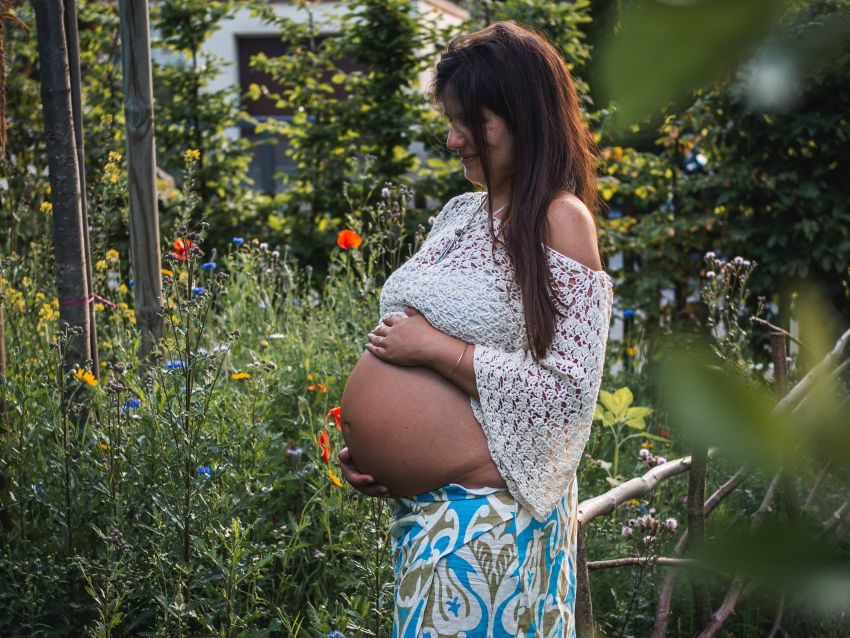 Schwangere Frau in einem Garten, die sanft ihren Bauch hält, umgeben von Blumen. Babybauchshooting in und um Geretsried