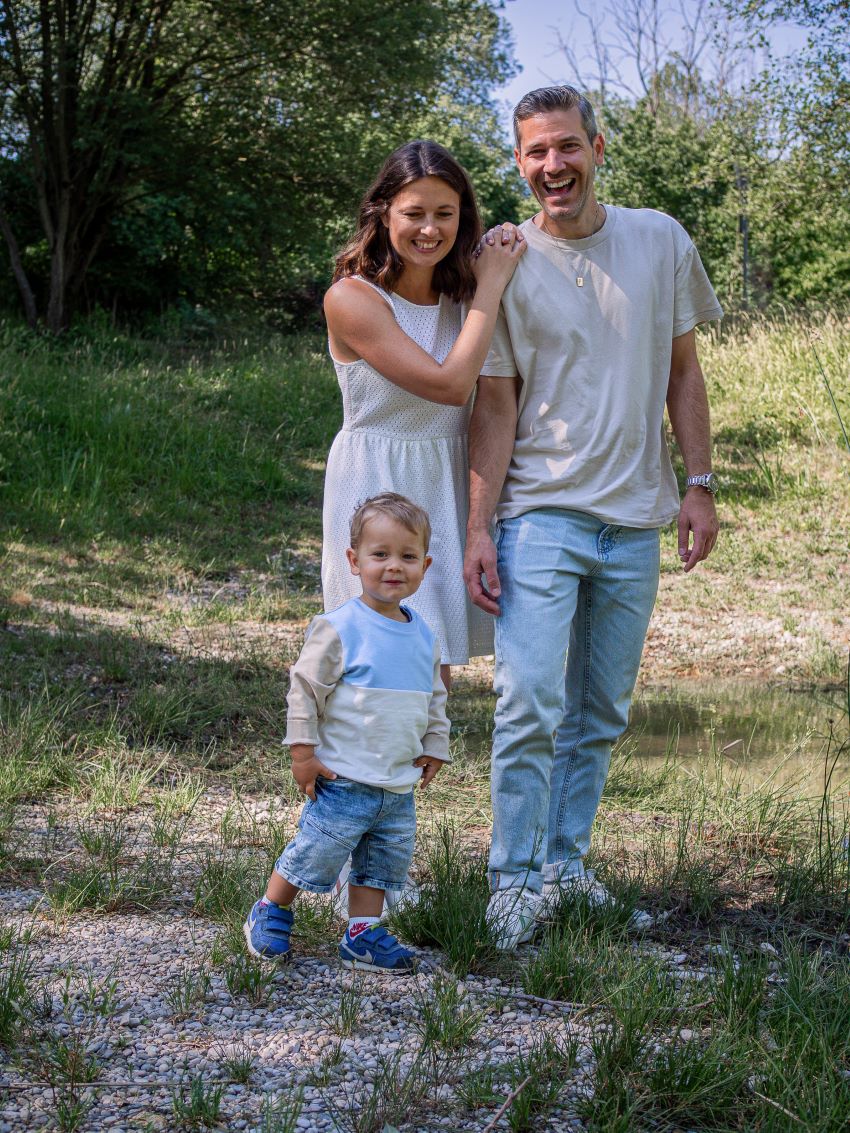 Familie mit kleinem Kind in der Natur, lächelnd und Hand in Hand stehend.