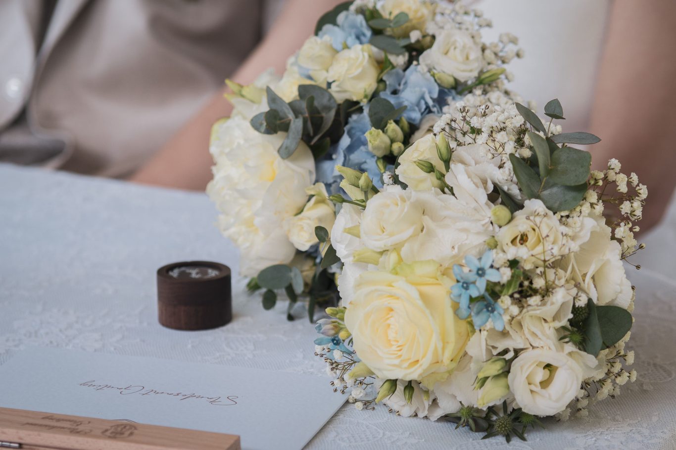 Hochzeit Detailaufnahme des Brautstraußes, er liegt neben einer kleinen Holzbox mit Eheringen und der Urkunde des Standesamts auf einem Tisch