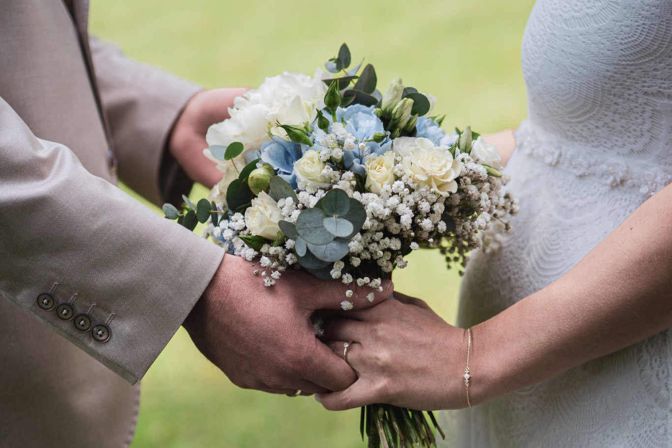 Hochzeit Detailaufnahme des Brautstraußes, das Brautpaar steht sich gegenüber und hält ihn gemeinsam in den Händen