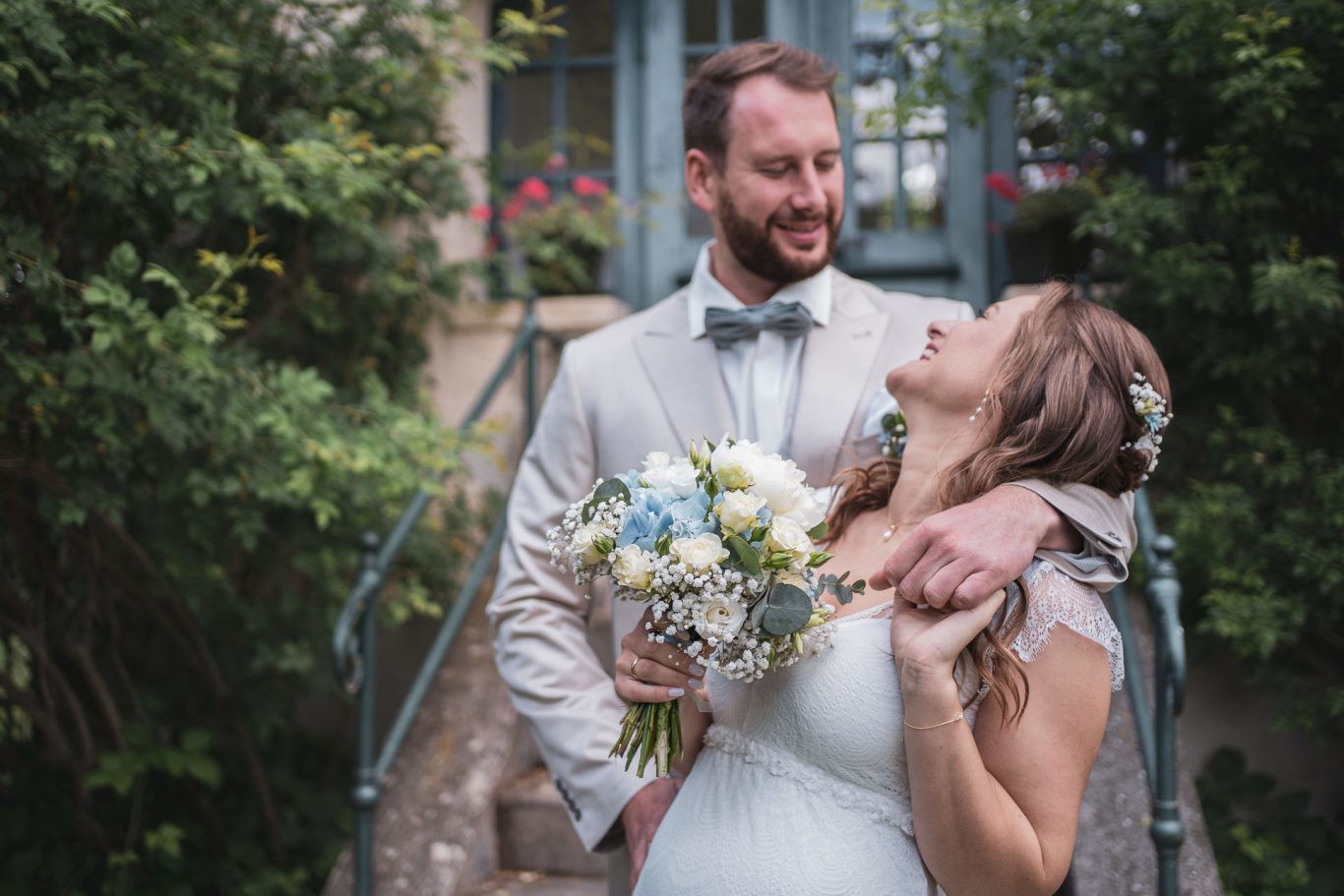 Hochzeit Ein festlich gekleidetes Brautpaar steht versetzt nebeneinander und lacht einander glücklich an, der Fokus liegt auf dem Brautstrauß